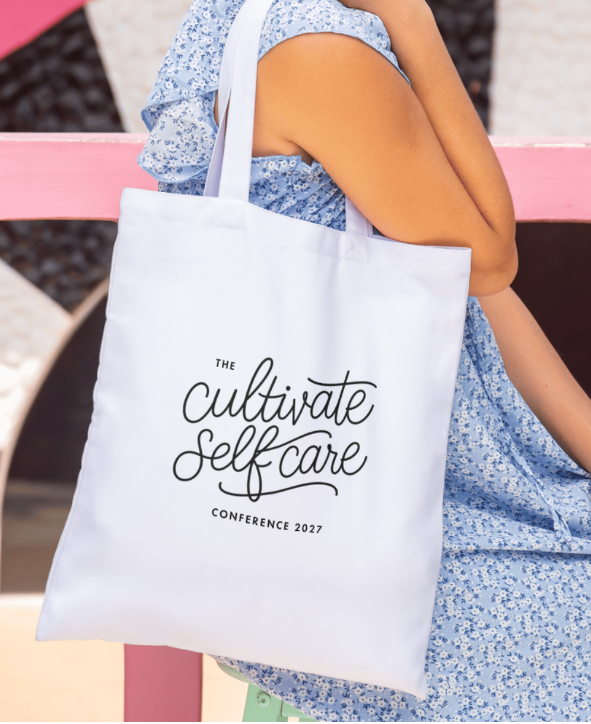Person holding a white tote bag with 'The Cultivate Self Care Conference 2027' text.