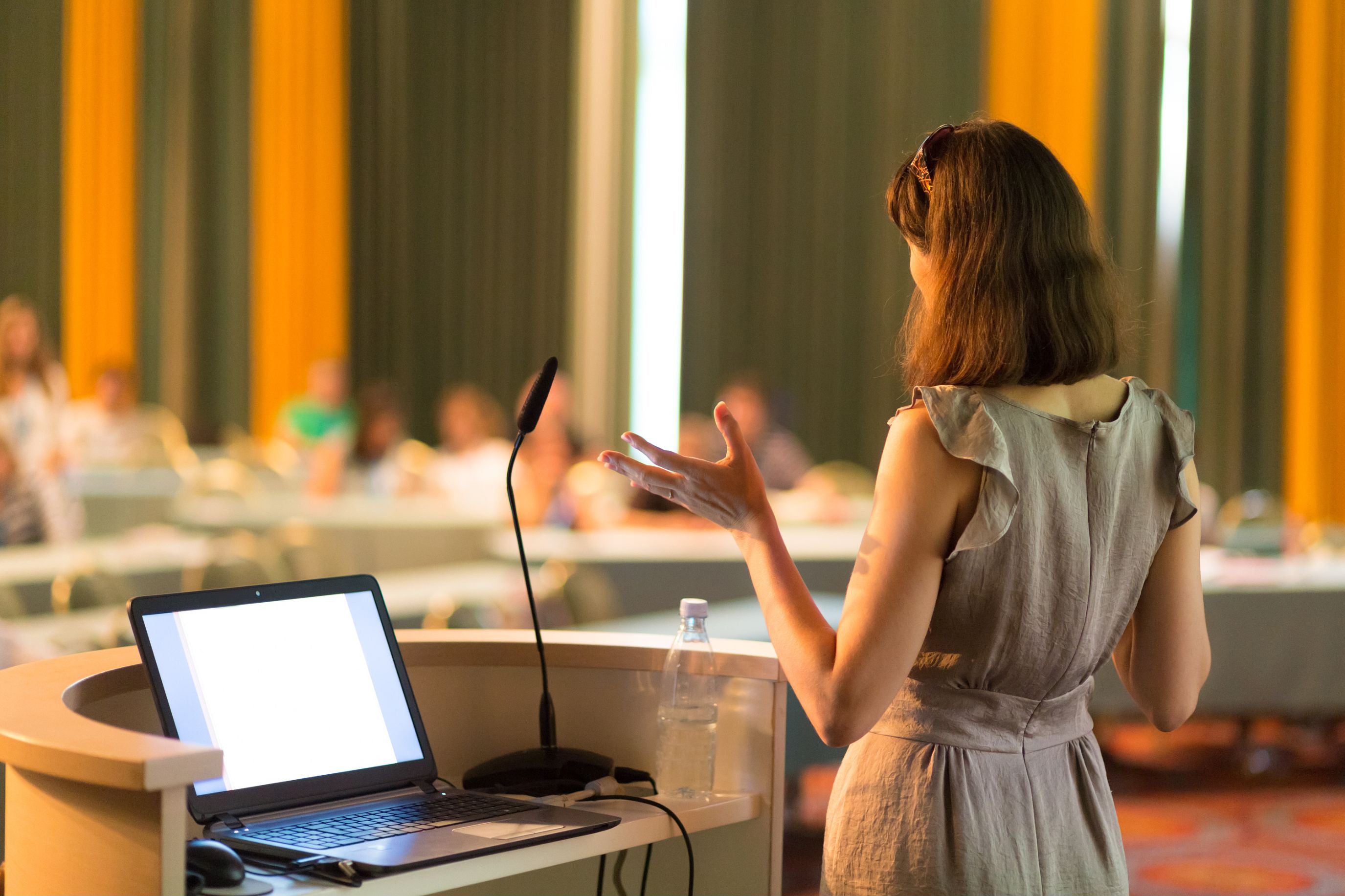 Woman giving a presentation in a conference room with a laptop on a podium.